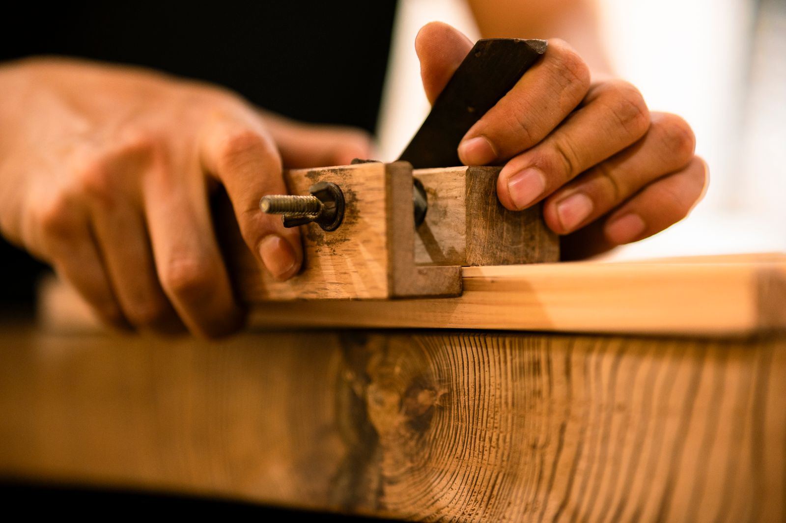 A woodworker's hands guiding a hand plane along a board